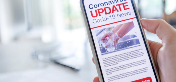 Close up of a mobile phone with Coronavirus covid-19 news update. The phone is being held and has an image of hand washing hygiene. There is paperwork on a table and home in the background. Copy space Pass sanitaire et obligation vaccinale : mise à jour du questions-réponses