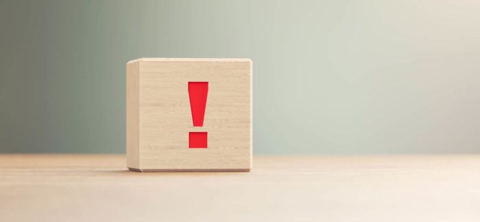 Exclamation point written wood block sitting on wood surface in front of a defocused background. Horizontal composition with copy space. Le ministère du Travail précise les conditions de recours à l’activité partielle pour les salariés d’entreprises affectées par des coupures électriques liées à un délestage